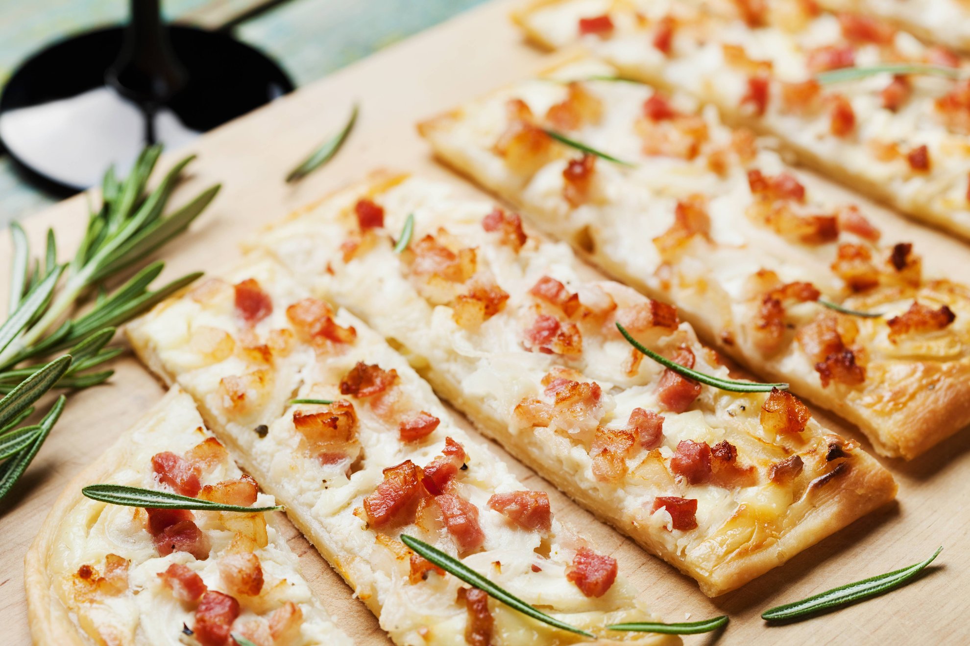 Flammkuchen Nahaufnahme Flammkuchen mit Speck und Rosmarin auf einem Holzbrett